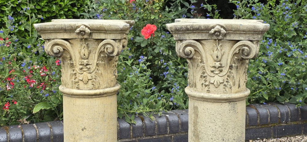 A pair of weathered buff cast stone Corinthian columns featuring acanthus leaf capitals and square bases. View III