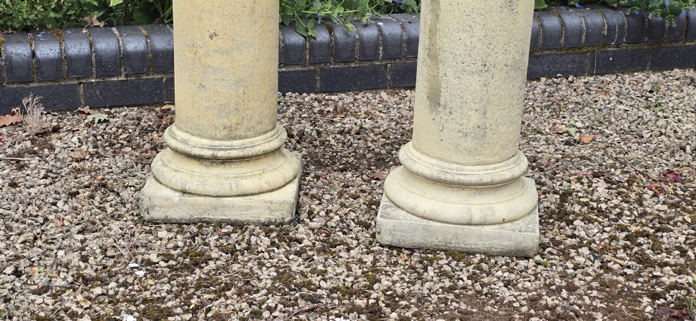 A pair of weathered buff cast stone Corinthian columns featuring acanthus leaf capitals and square bases. View IV