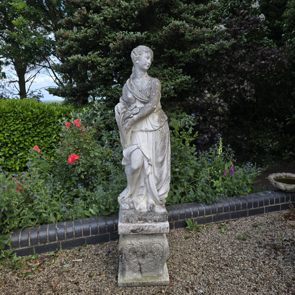 A full-length cast stone statue of a classical draped female figure standing atop a square carved plinth base.