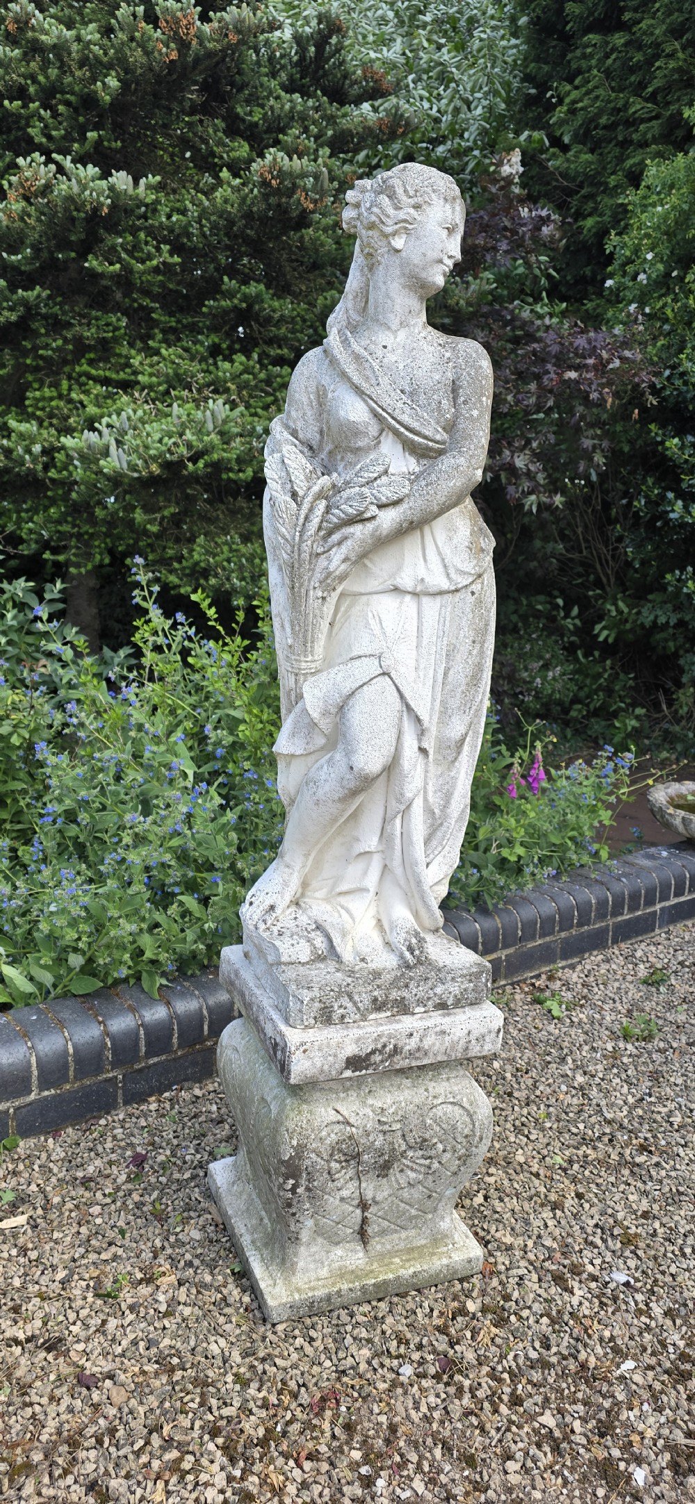 A full-length cast stone statue of a classical draped female figure standing atop a square carved plinth base. View II