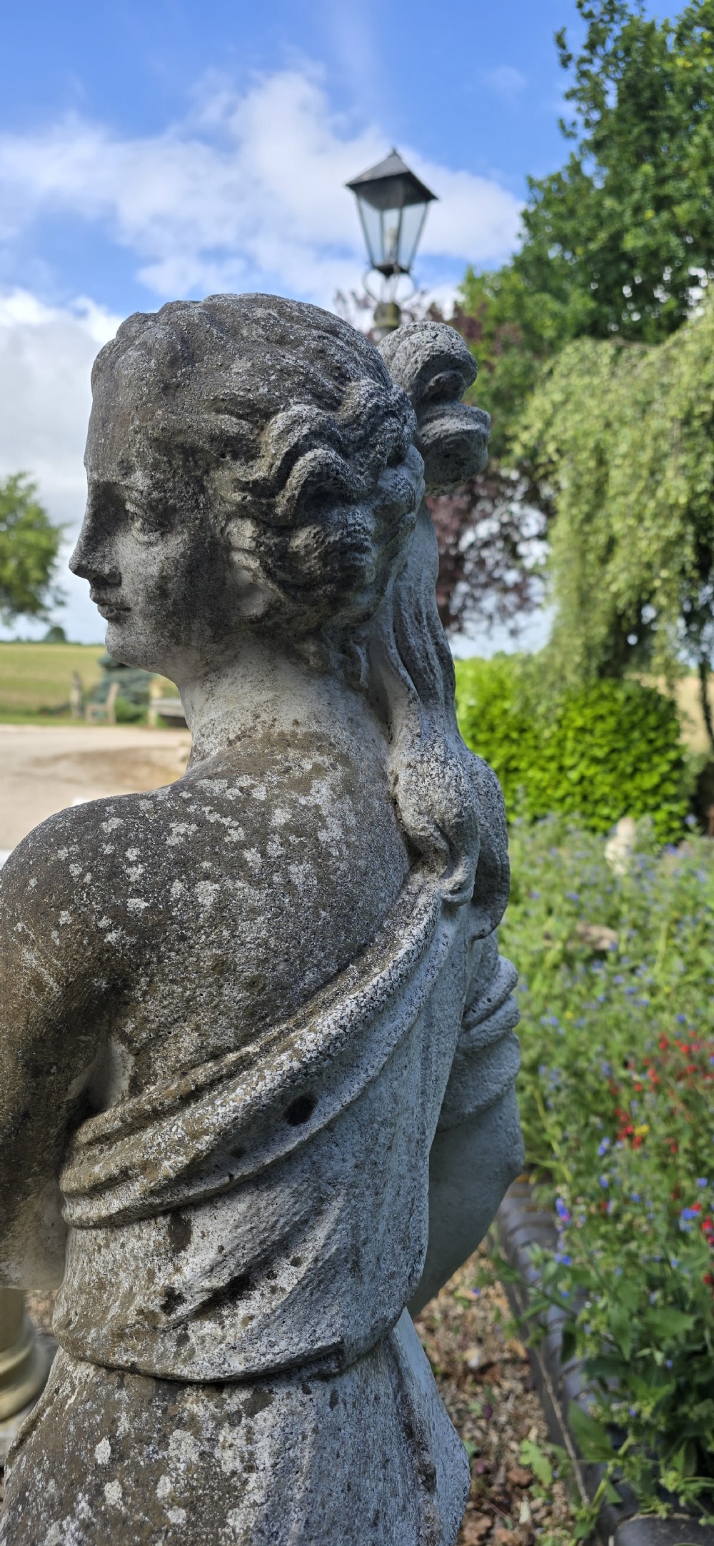 A full-length cast stone statue of a classical draped female figure standing atop a square carved plinth base. View V