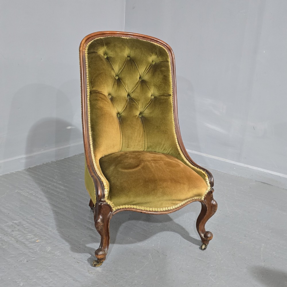 An antique low-seated slipper chair with olive green deep-buttoned velvet upholstery, a moulded mahogany frame, and cabriole front legs on brass castors.
