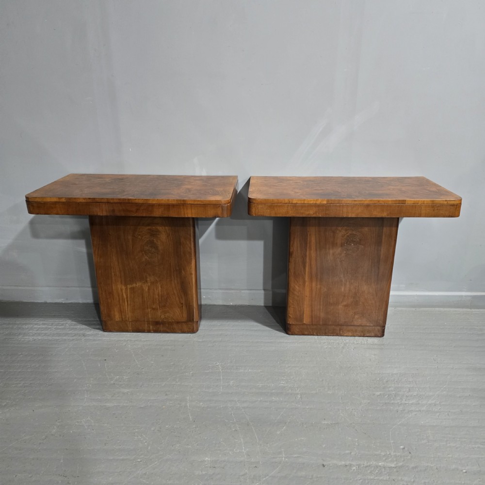 A pair of Art Deco console tables crafted from figured burr walnut, featuring overhanging rectangular tops with rounded edges set on thick rectangular pedestal bases.
