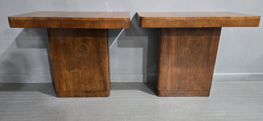 A pair of Art Deco console tables crafted from figured burr walnut, featuring overhanging rectangular tops with rounded edges set on thick rectangular pedestal bases. View VI