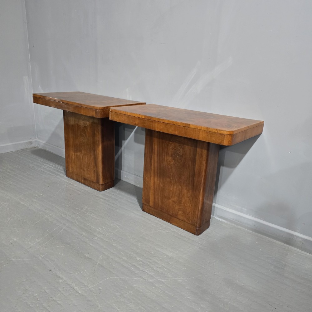 A pair of Art Deco console tables crafted from figured burr walnut, featuring overhanging rectangular tops with rounded edges set on thick rectangular pedestal bases. View VII