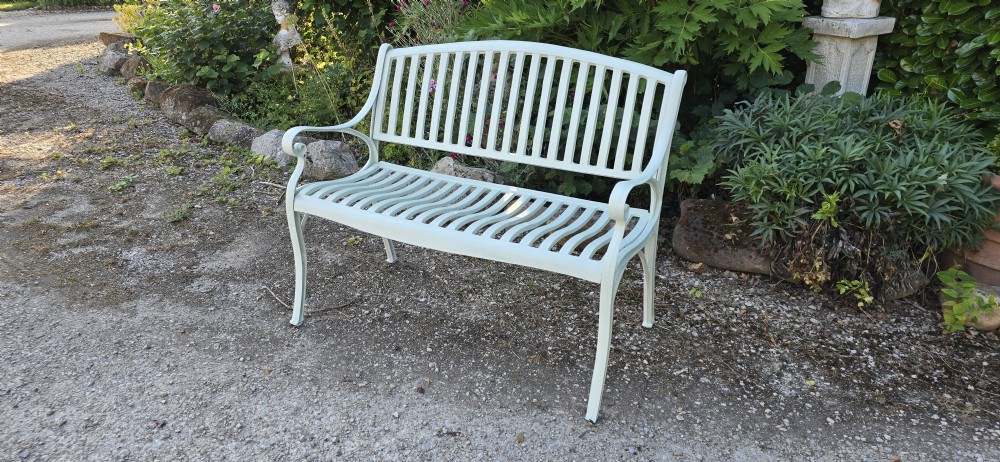 A pale green painted metal garden bench featuring a vertical slatted arched backrest, horizontal slatted seat, and curved armrests. View II