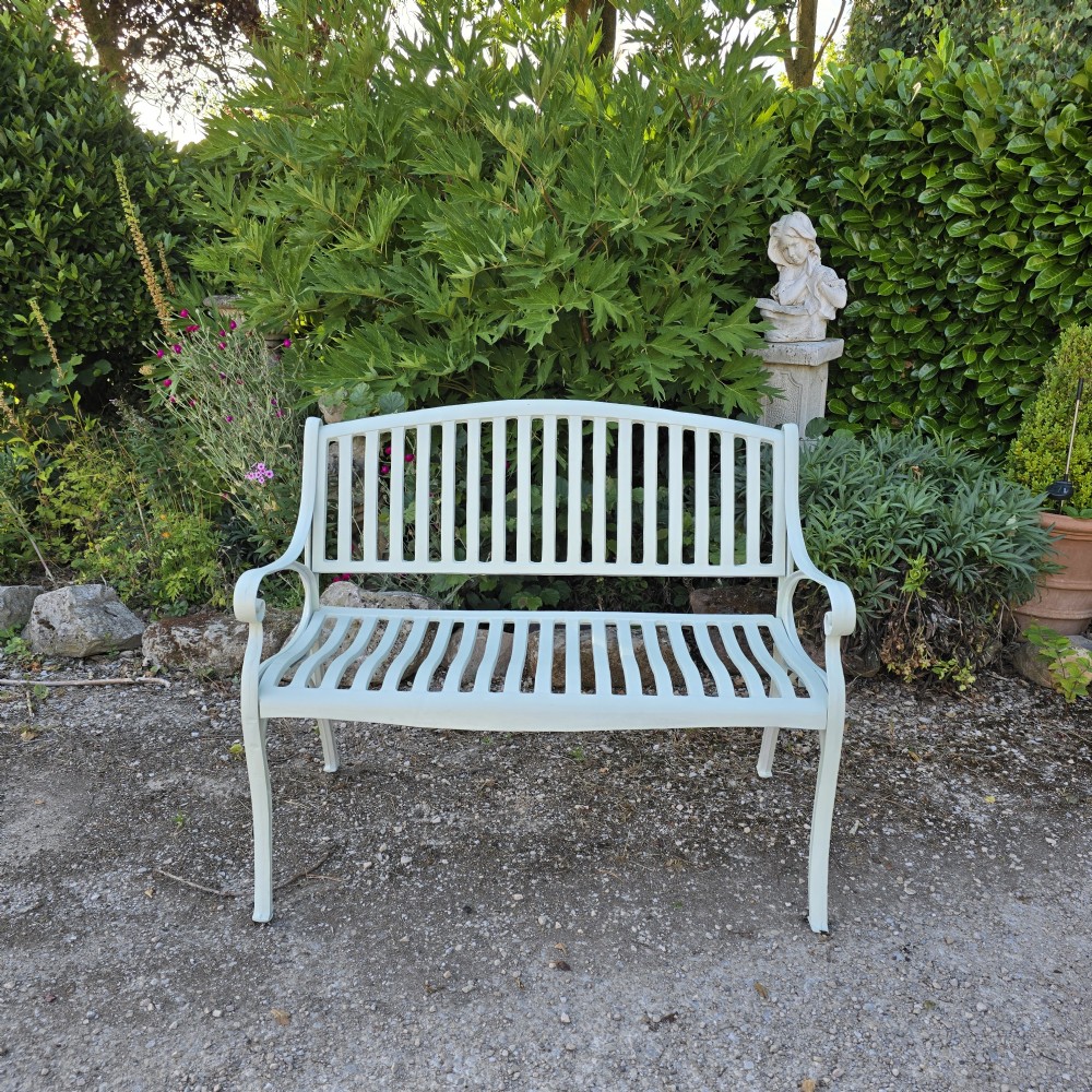 A pale green painted metal garden bench featuring a vertical slatted arched backrest, horizontal slatted seat, and curved armrests. View III