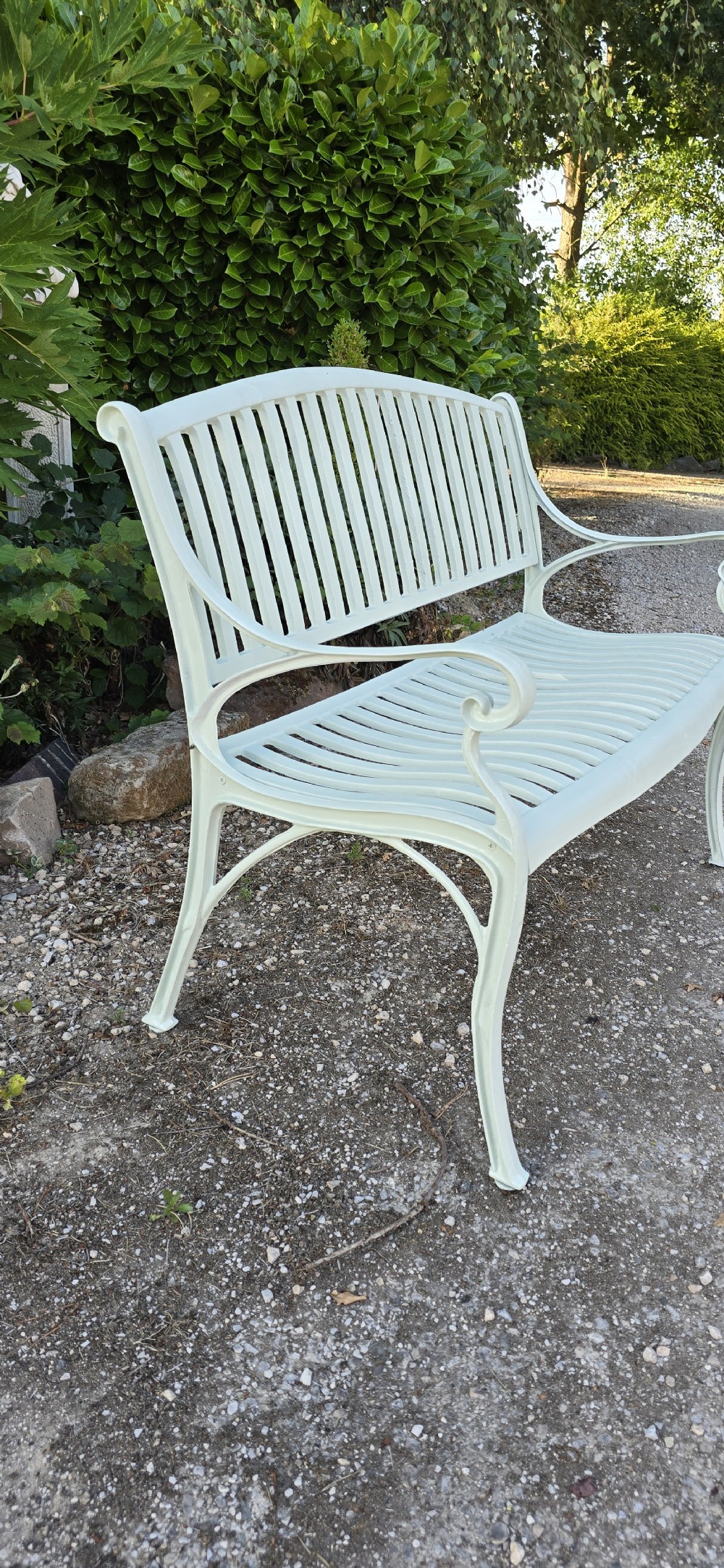 A pale green painted metal garden bench featuring a vertical slatted arched backrest, horizontal slatted seat, and curved armrests. View V
