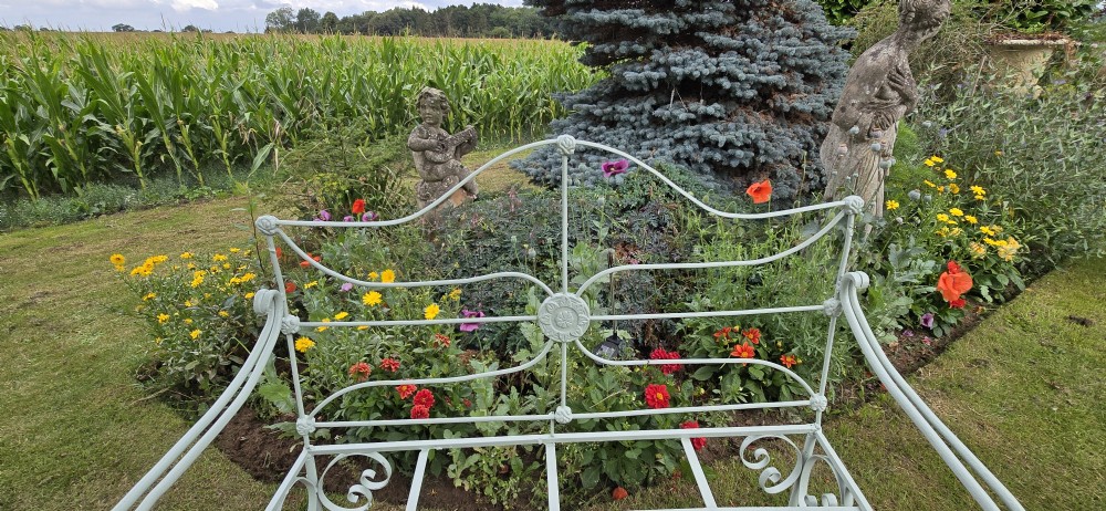 A sage green painted wrought iron garden bench featuring scrolled armrests, an arched backrest with a central rosette medallion, and an open metal grid seat. View VIII