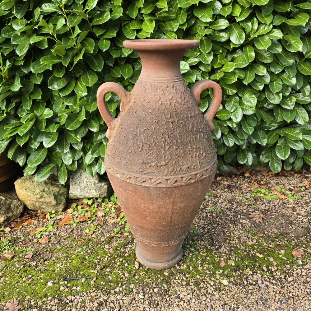 A large terracotta oil jar with two side handles, a textured upper body, and incised geometric patterning.