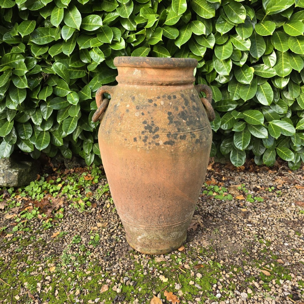 A weathered terracotta oil jar featuring a thick rolled rim, twin loop handles on the shoulders, and aged surface discolouration.