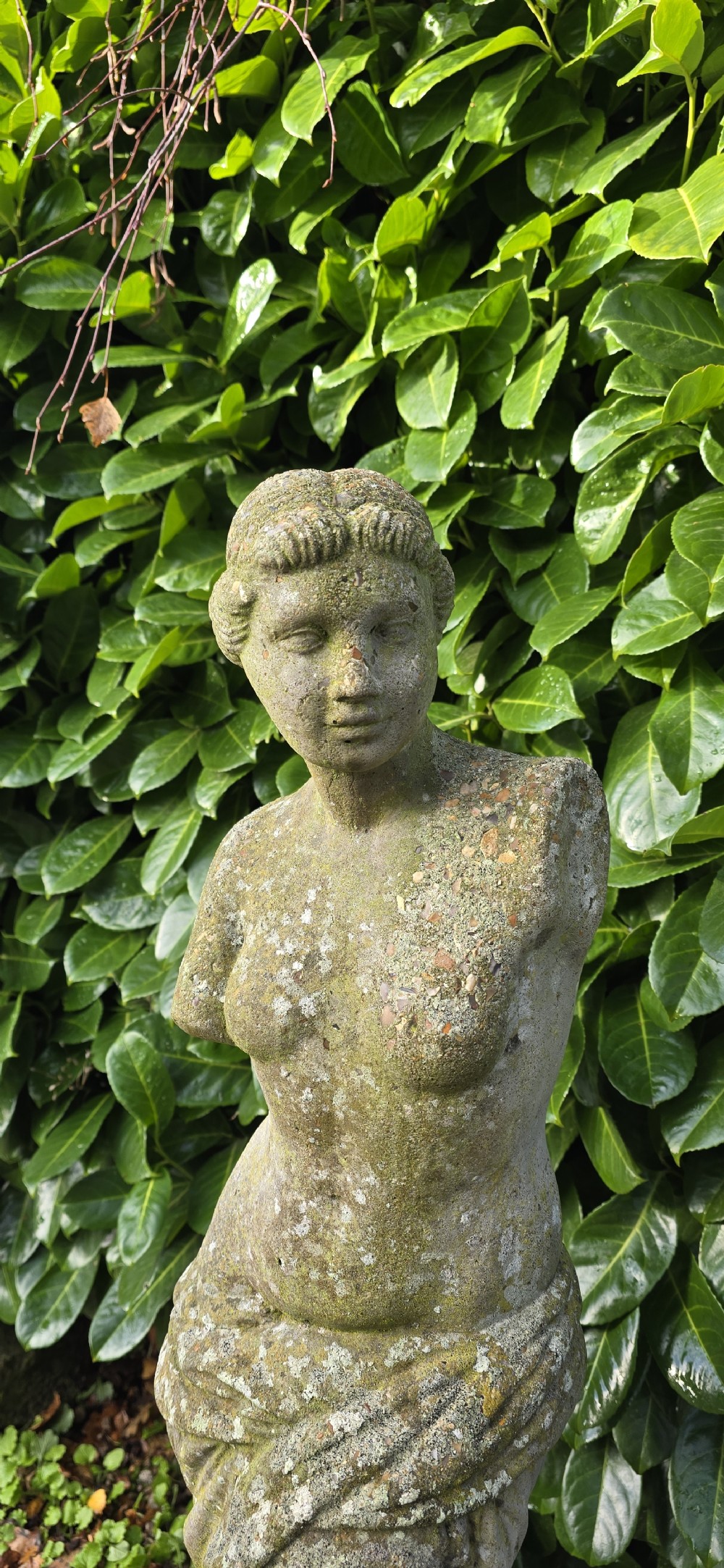 A weathered cast stone statue depicting the armless Venus de Milo draped in cloth on a square plinth. View V