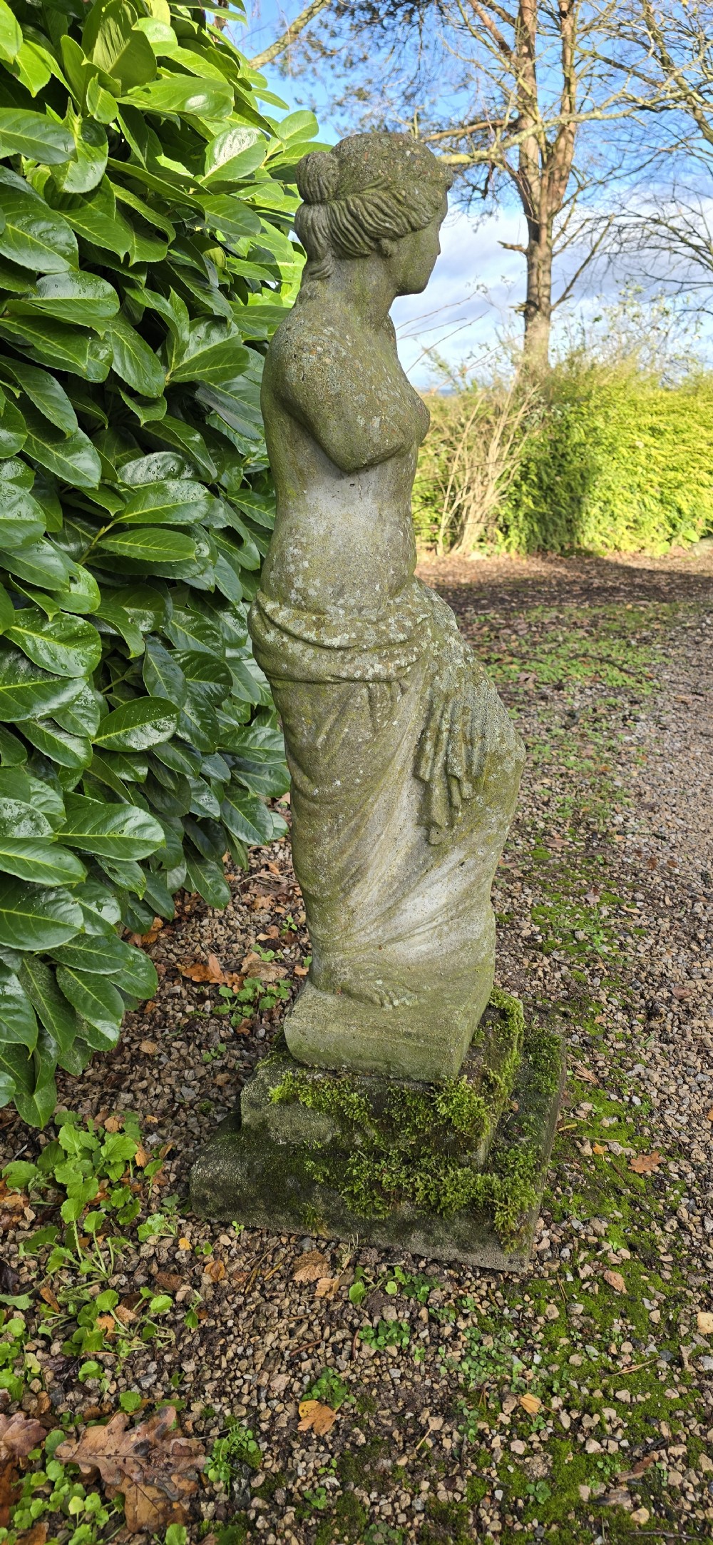A weathered cast stone statue depicting the armless Venus de Milo draped in cloth on a square plinth. View VI