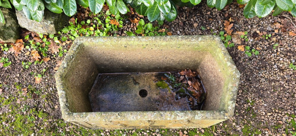 A rectangular composite stone garden trough featuring raised relief carvings of three figures in 18th-century dress on the front panel with a weathered surface. View III