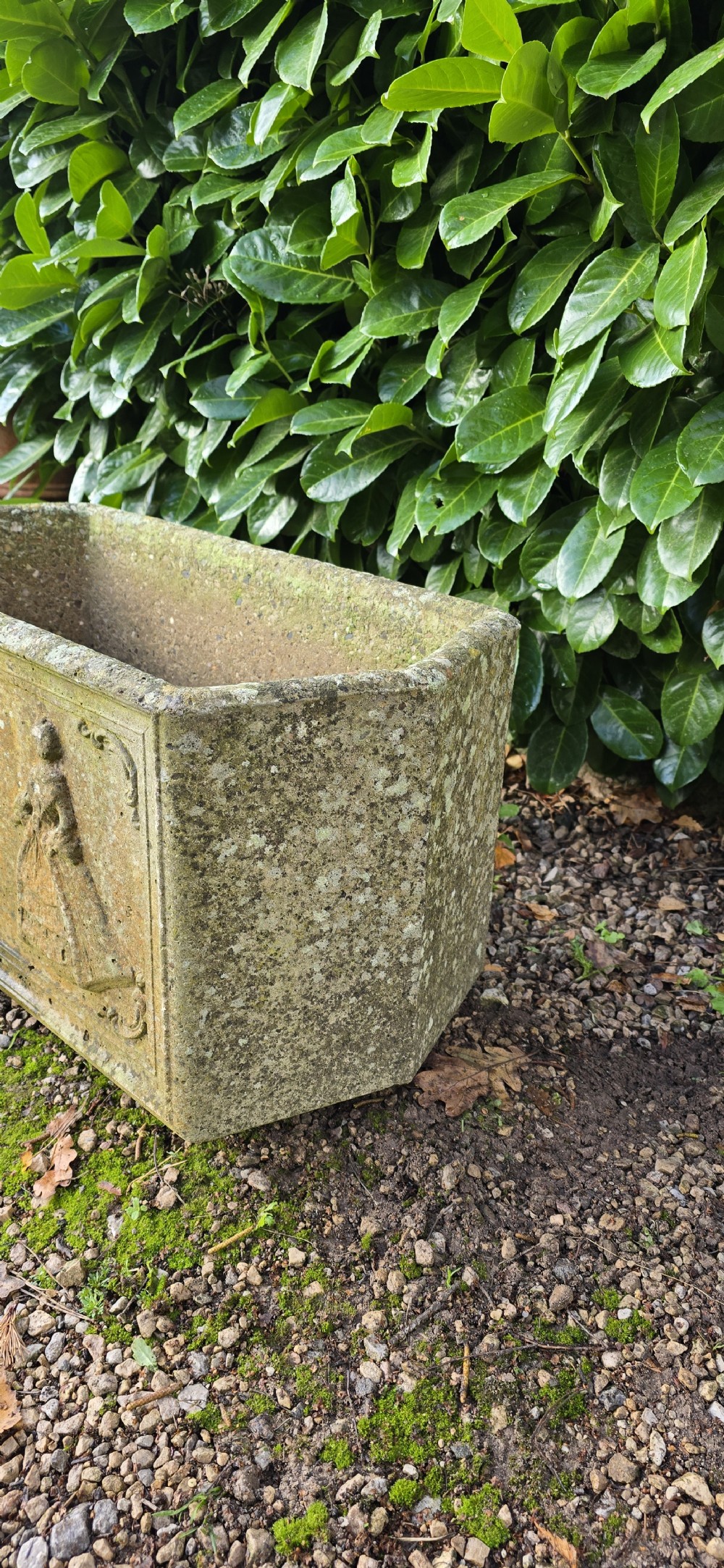 A rectangular composite stone garden trough featuring raised relief carvings of three figures in 18th-century dress on the front panel with a weathered surface. View IV
