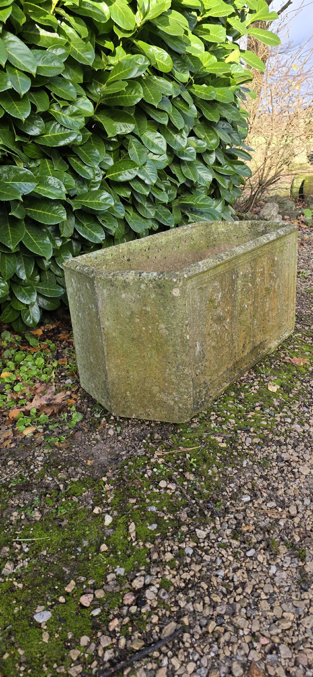 A rectangular composite stone garden trough featuring raised relief carvings of three figures in 18th-century dress on the front panel with a weathered surface. View V