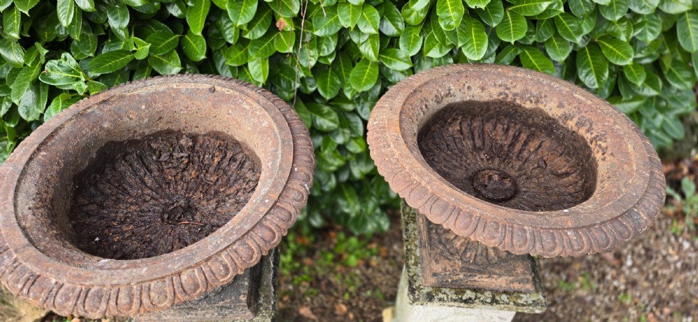 A pair of weathered cast iron garden urns with fluted rims resting on tall, square stone plinths. View VI