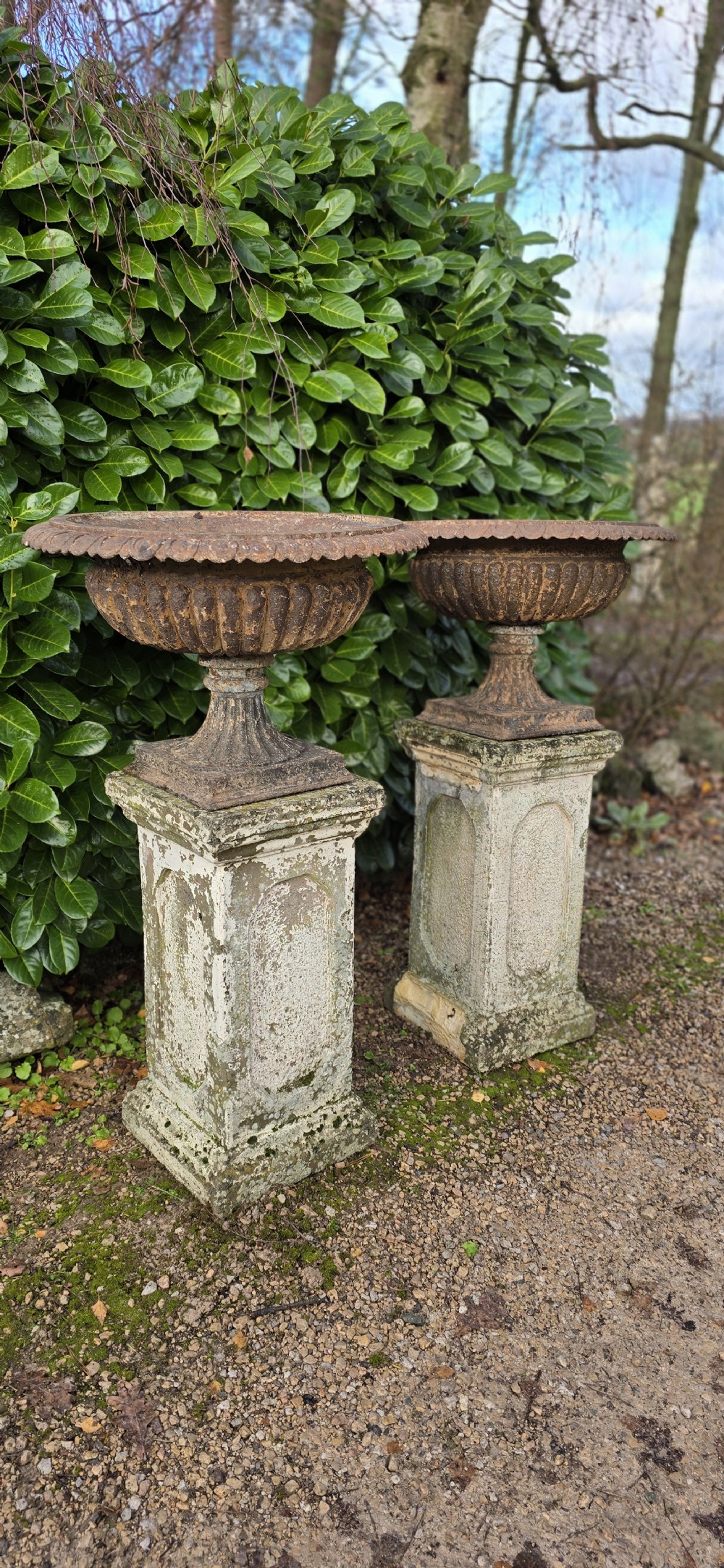 A pair of weathered cast iron garden urns with fluted rims resting on tall, square stone plinths. View VIII
