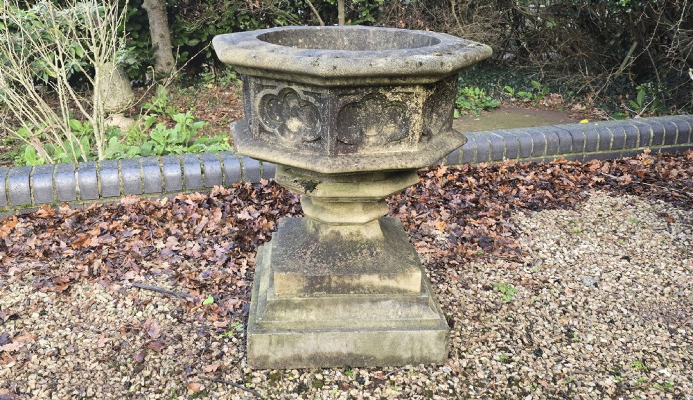 A weathered heptagonal cast stone garden urn featuring carved Gothic tracery panels resting on a stepped pedestal base. View IV
