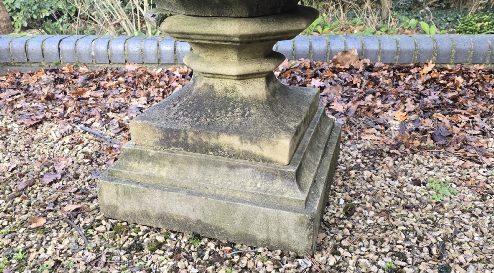 A weathered heptagonal cast stone garden urn featuring carved Gothic tracery panels resting on a stepped pedestal base. View VI