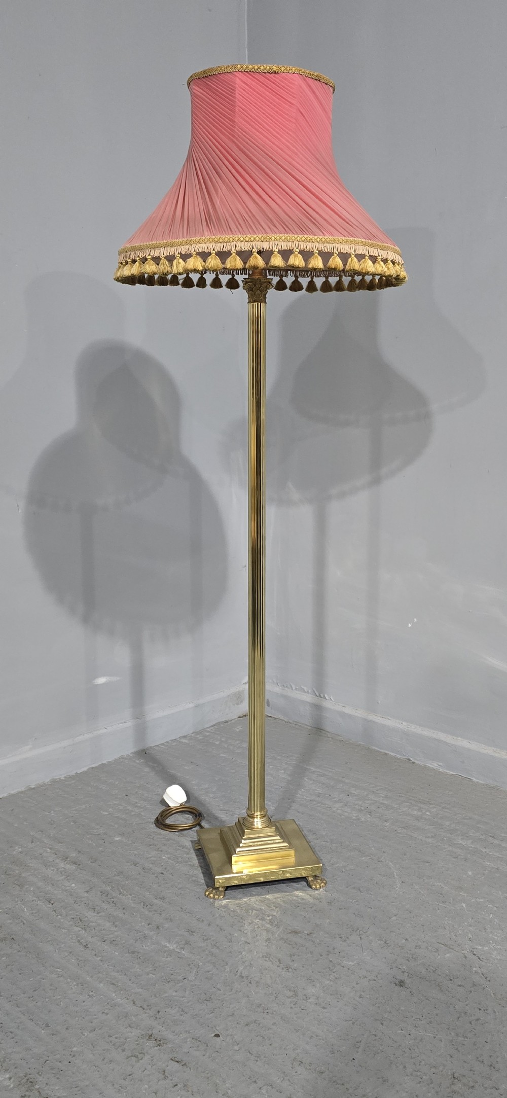 A solid brass standard lamp featuring a fluted Corinthian column stem, stepped square base on paw feet, and a pleated pink fabric shade with tassel fringe. View IX