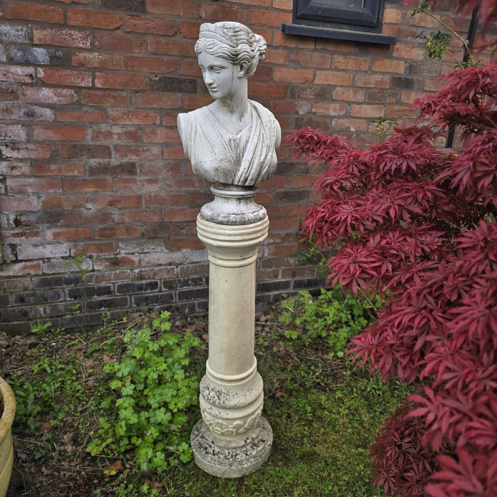 A weathered cast stone bust of classical goddess Athena set atop a turned cylindrical stone plinth.