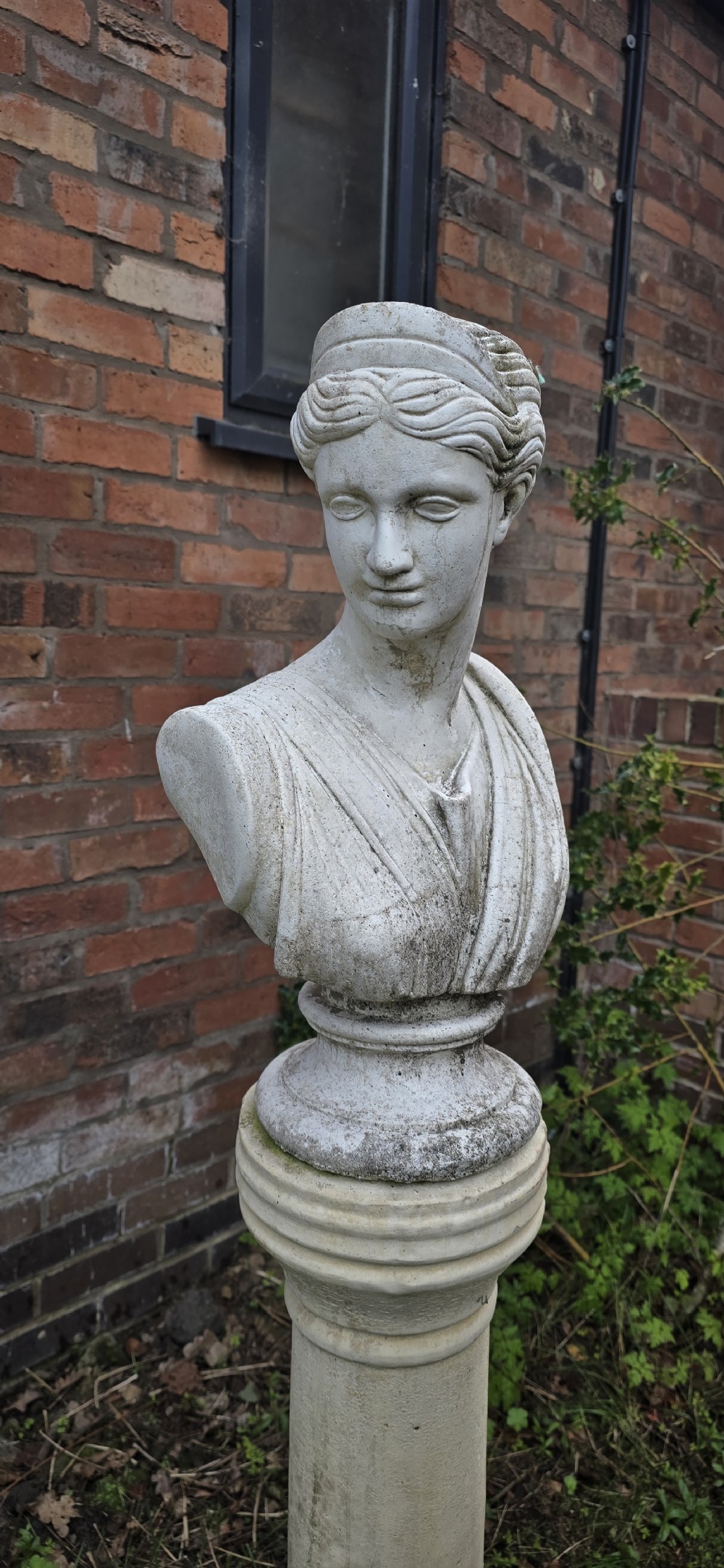 A weathered cast stone bust of classical goddess Athena set atop a turned cylindrical stone plinth. View IV