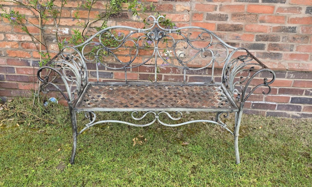 A French metal garden bench featuring a weathered grey-green painted finish, decorative scrollwork backrest, rolled arms, and a lattice seat. View II