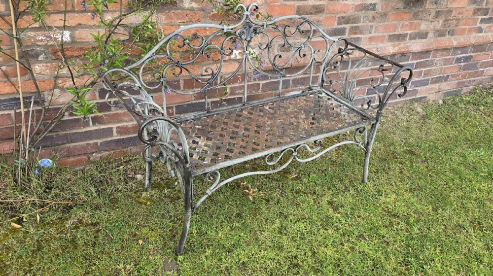 A French metal garden bench featuring a weathered grey-green painted finish, decorative scrollwork backrest, rolled arms, and a lattice seat. View III