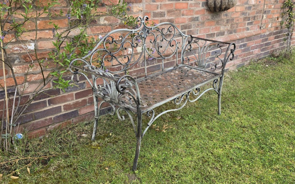 A French metal garden bench featuring a weathered grey-green painted finish, decorative scrollwork backrest, rolled arms, and a lattice seat. View V