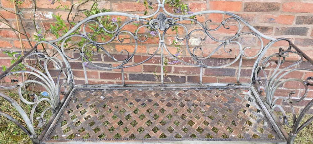 A French metal garden bench featuring a weathered grey-green painted finish, decorative scrollwork backrest, rolled arms, and a lattice seat. View VI