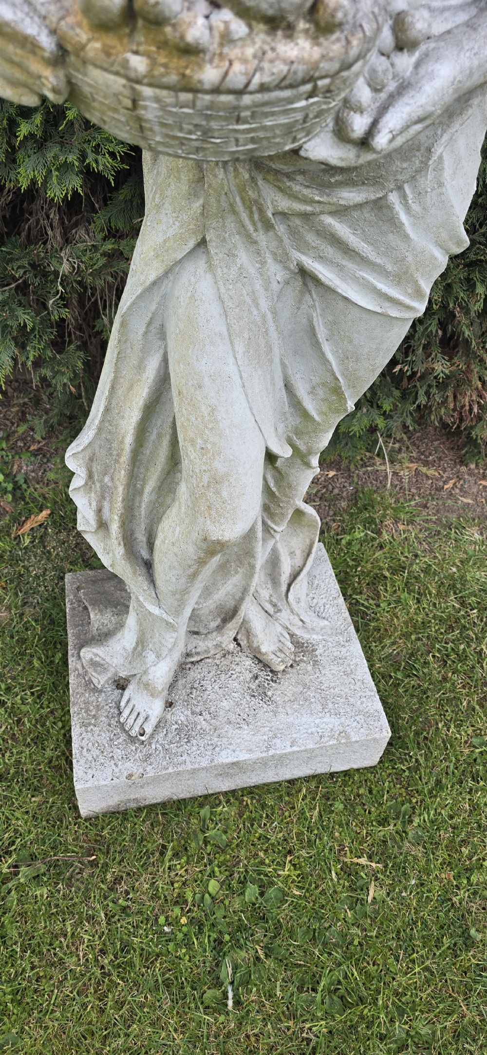 A life-sized classical stone garden statue of a draped female figure holding a basket of fruit on a square base. View V