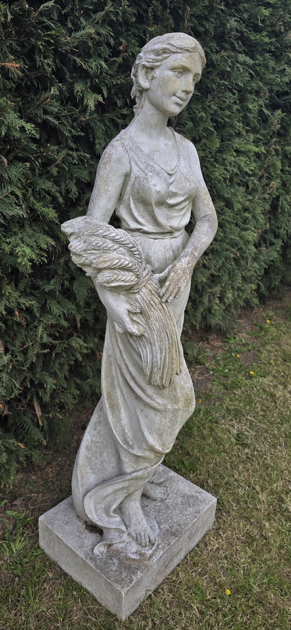 A life-sized weathered stone classical garden statue representing summer, featuring a draped female figure holding a sheaf of wheat on a square plinth base. View III