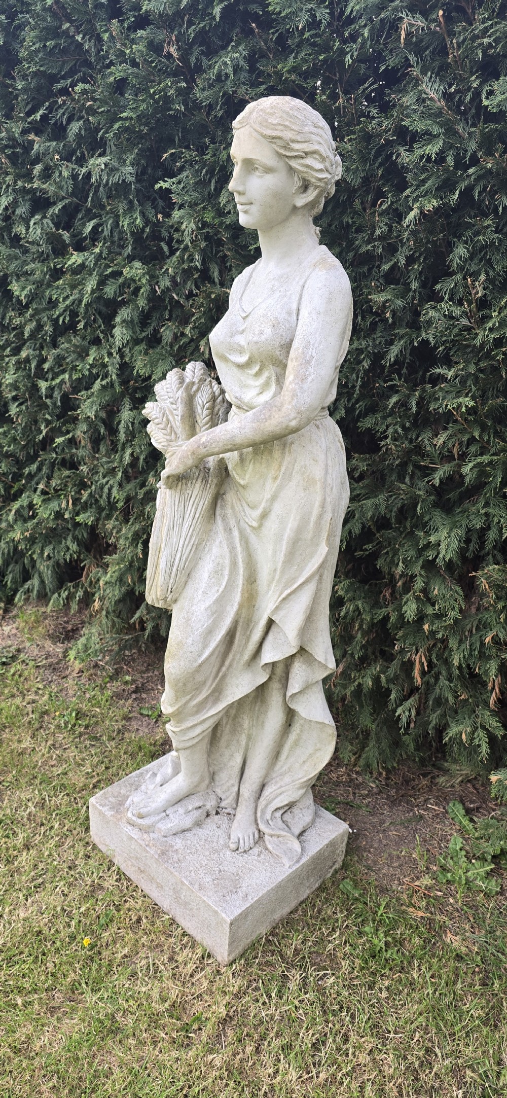 A life-sized weathered stone classical garden statue representing summer, featuring a draped female figure holding a sheaf of wheat on a square plinth base. View IV