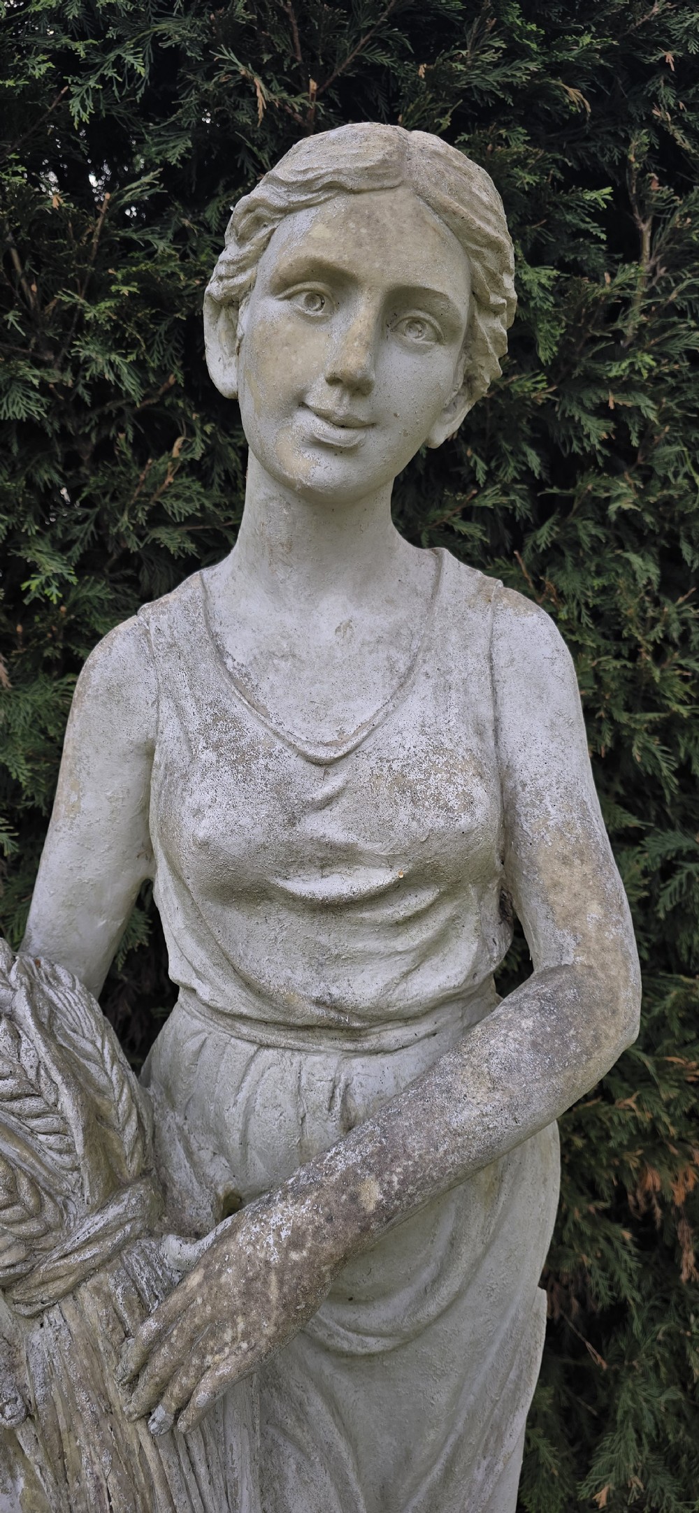 A life-sized weathered stone classical garden statue representing summer, featuring a draped female figure holding a sheaf of wheat on a square plinth base. View V