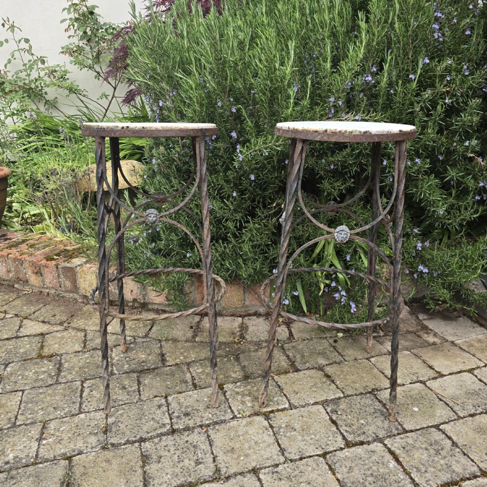 A pair of tall wrought iron plant stands with circular stone tops, twisted legs, and central lion mask medallion details. View II