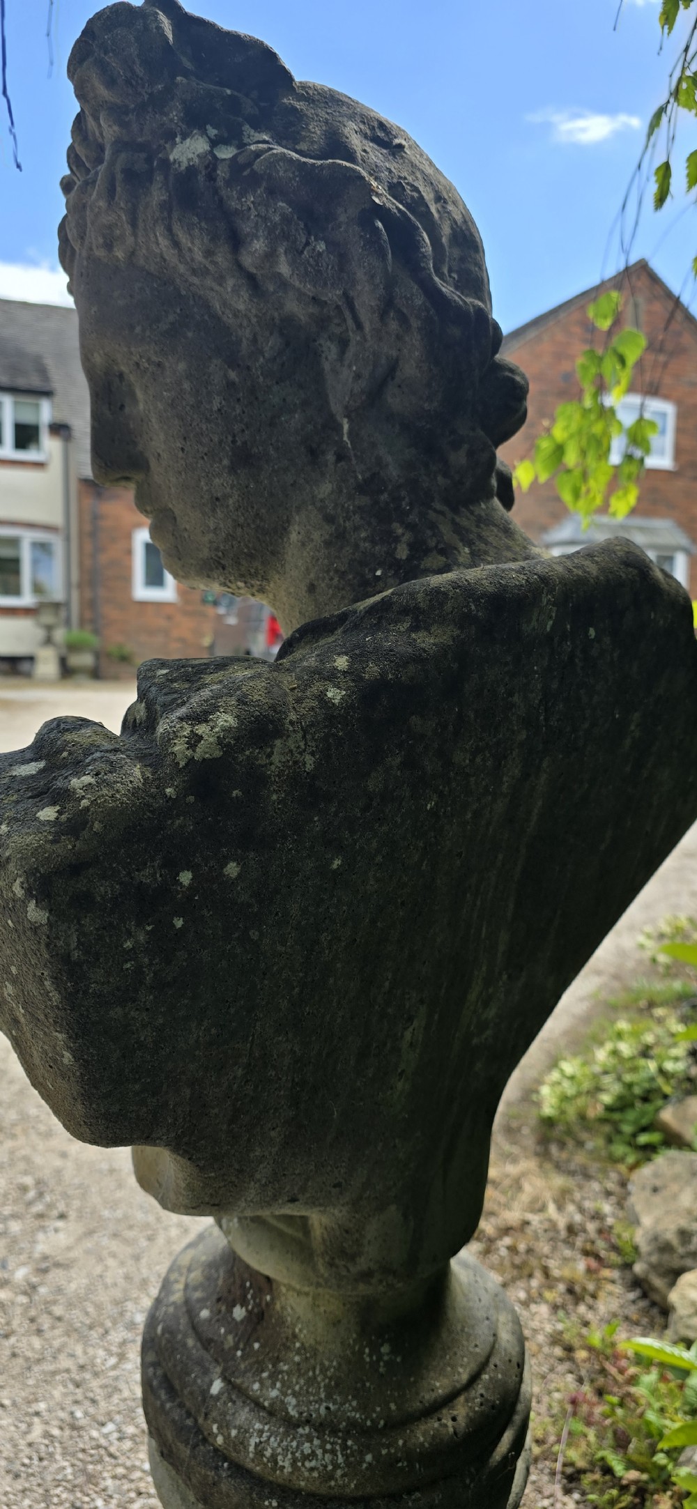 A weathered stone bust of Apollo set atop a cylindrical column pedestal with a square base. View V