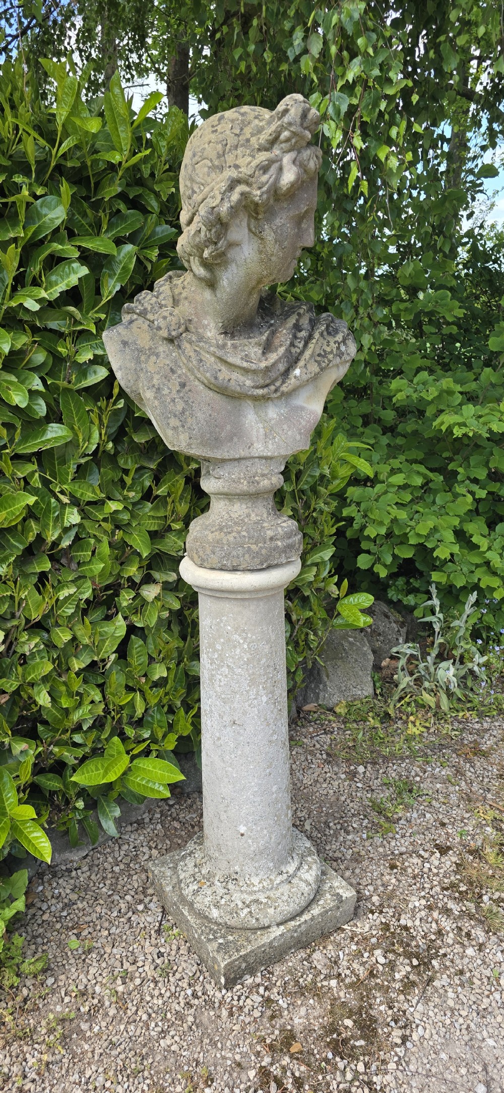 A weathered stone bust of Apollo set atop a cylindrical column pedestal with a square base. View VII
