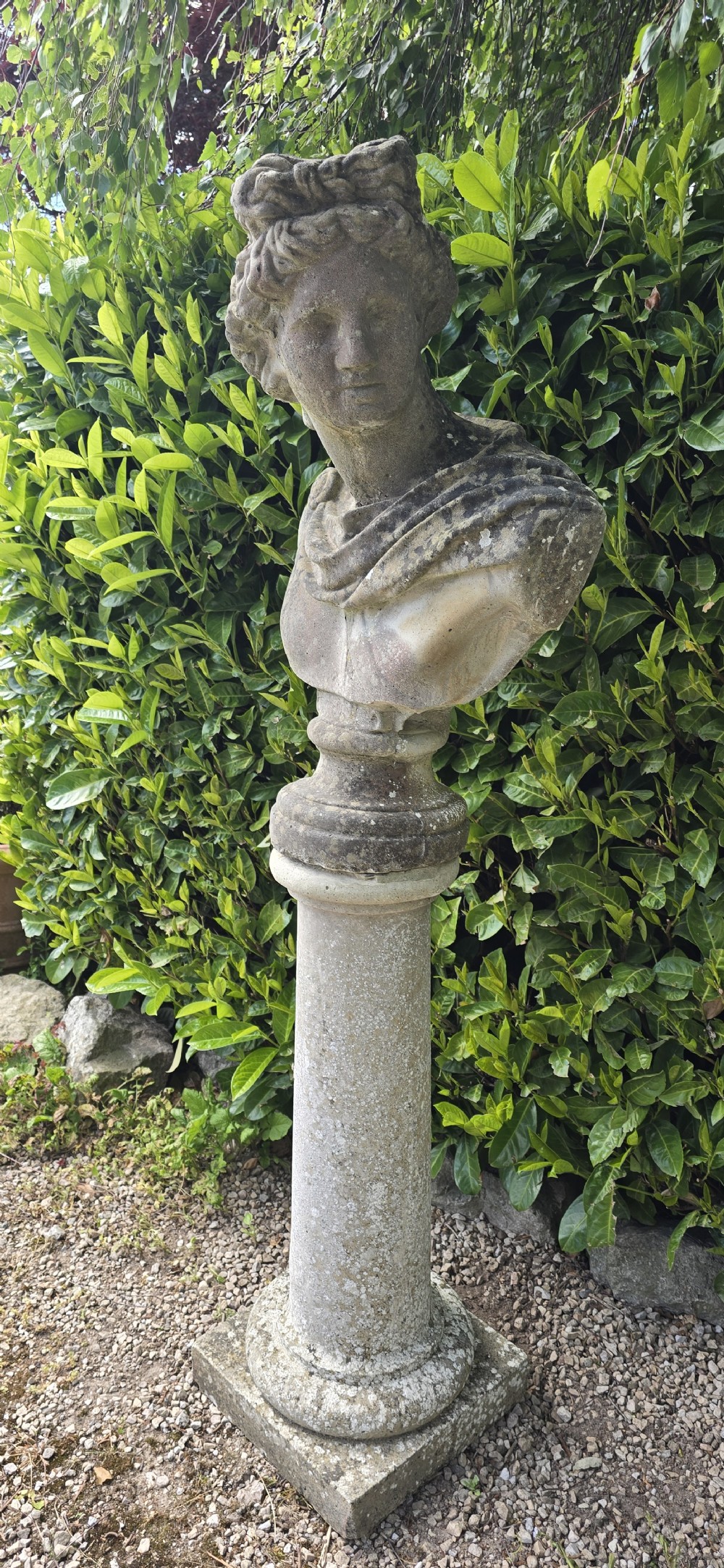 A weathered stone bust of Apollo set atop a cylindrical column pedestal with a square base. View VIII