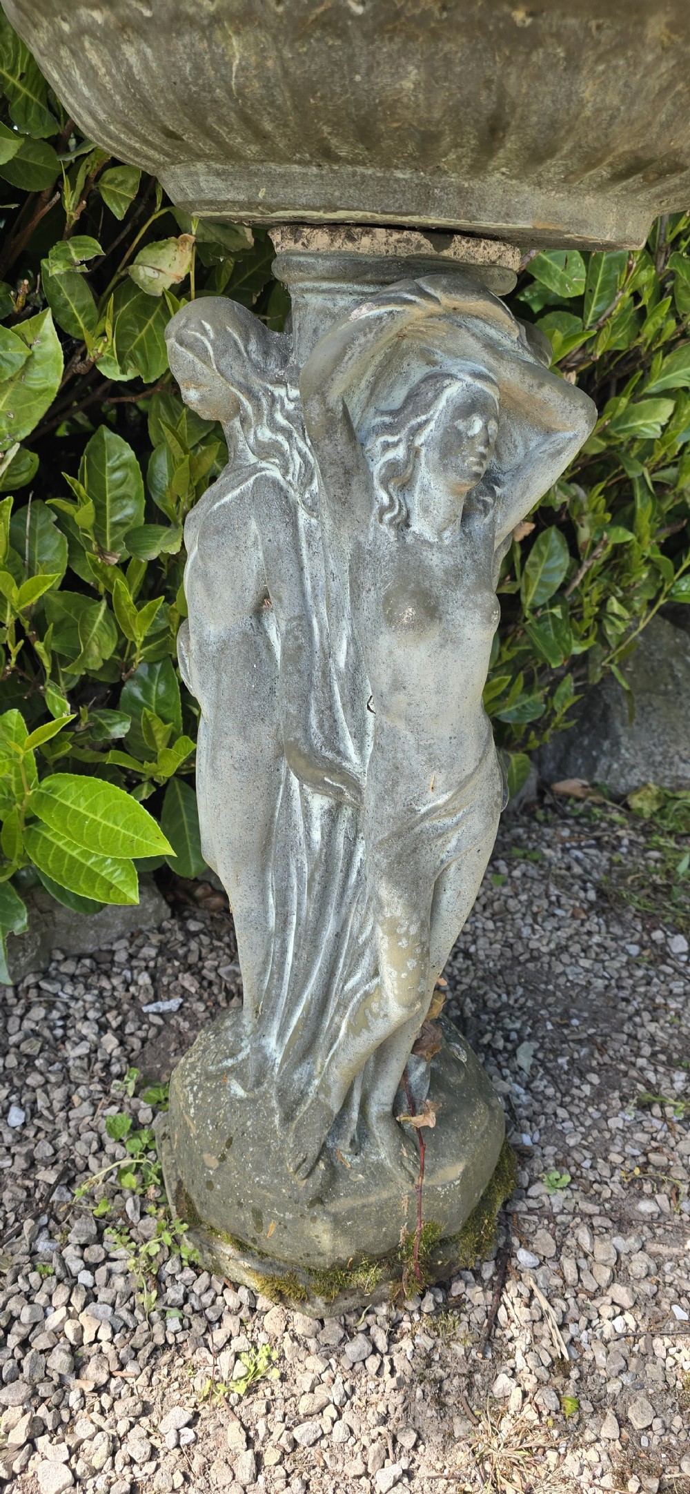 A weathered grey reconstituted stone bird bath featuring a circular top basin resting on a column supported by three draped female figures. View II