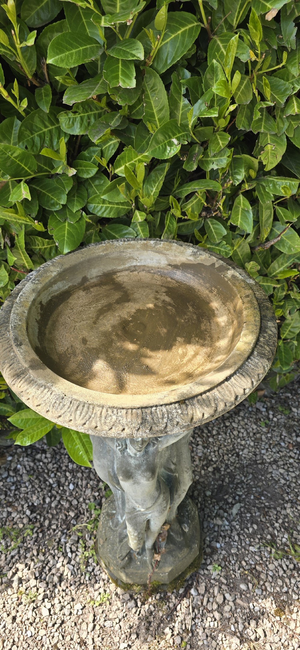 A weathered grey reconstituted stone bird bath featuring a circular top basin resting on a column supported by three draped female figures. View V