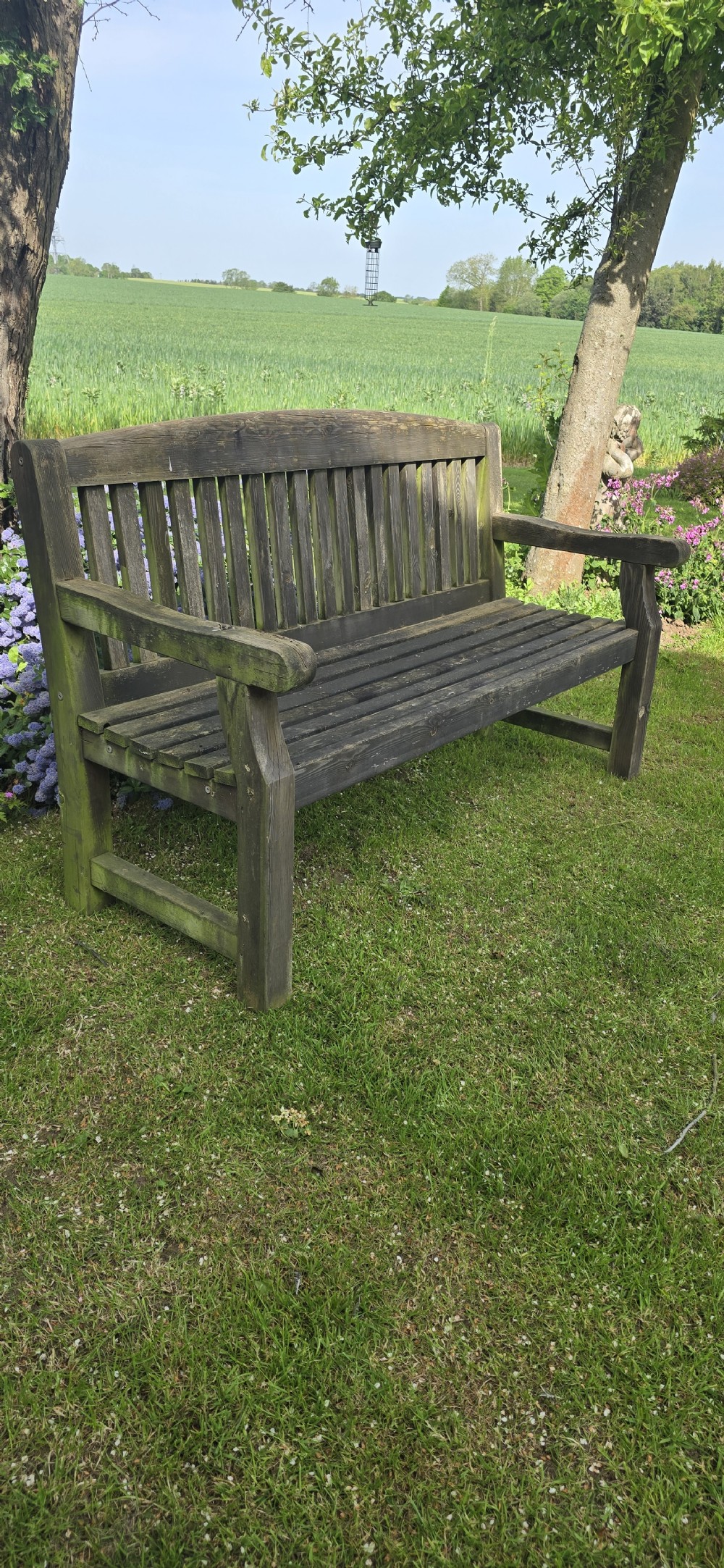 A weathered silver-grey teak garden bench featuring a slatted backrest, slatted seat, wide armrests, and straight post legs. View VI