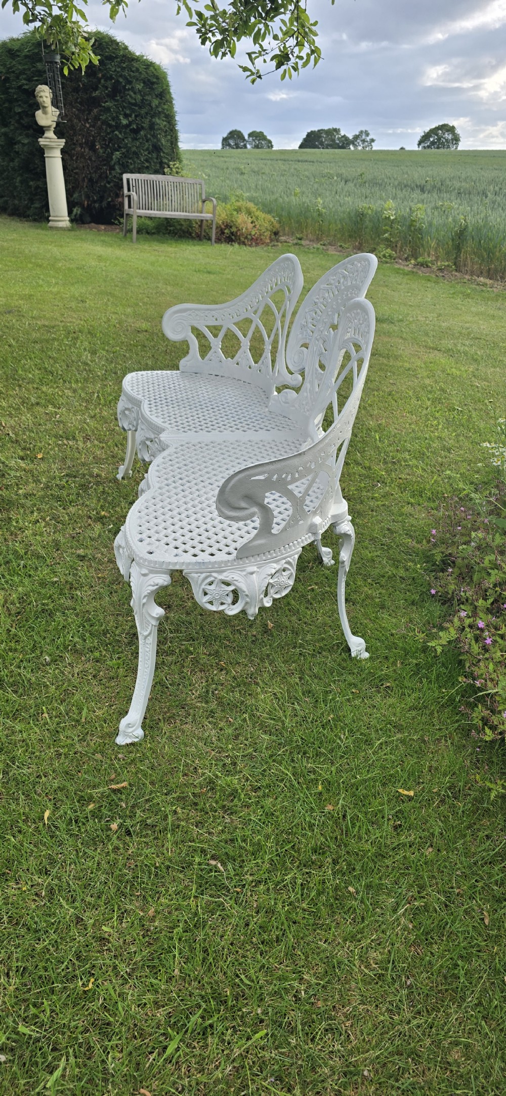 A refurbished white cast metal garden bench featuring an ornate lattice seat, three-part curved backrest with foliage motifs, and decorative legs. View III