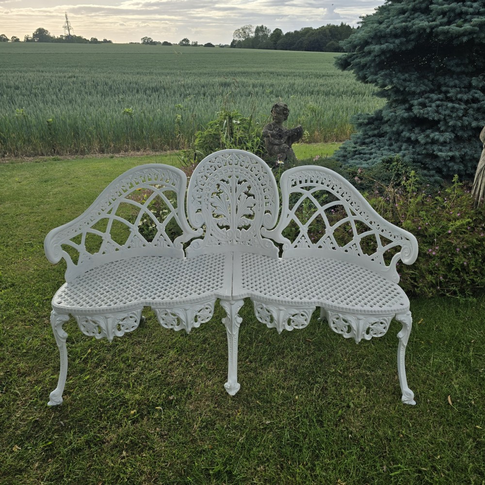 A refurbished white cast metal garden bench featuring an ornate lattice seat, three-part curved backrest with foliage motifs, and decorative legs.