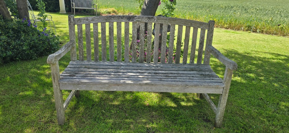 A weathered teak garden bench with a silvered grey patina, featuring vertical back slats, flat armrests, and square legs. View II