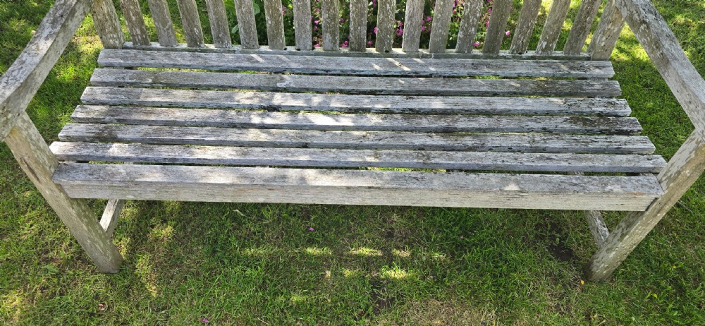 A weathered teak garden bench with a silvered grey patina, featuring vertical back slats, flat armrests, and square legs. View III