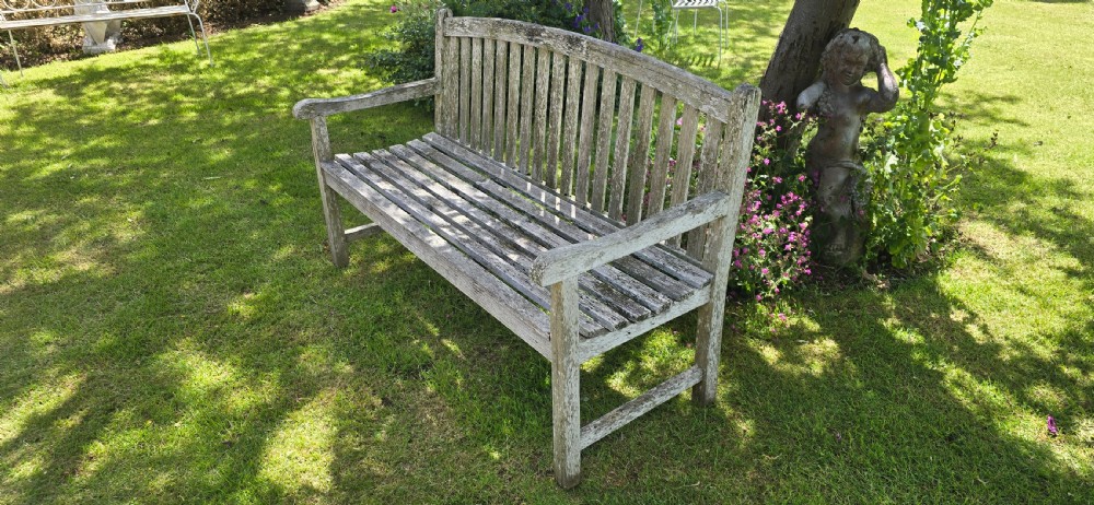 A weathered teak garden bench with a silvered grey patina, featuring vertical back slats, flat armrests, and square legs. View IV