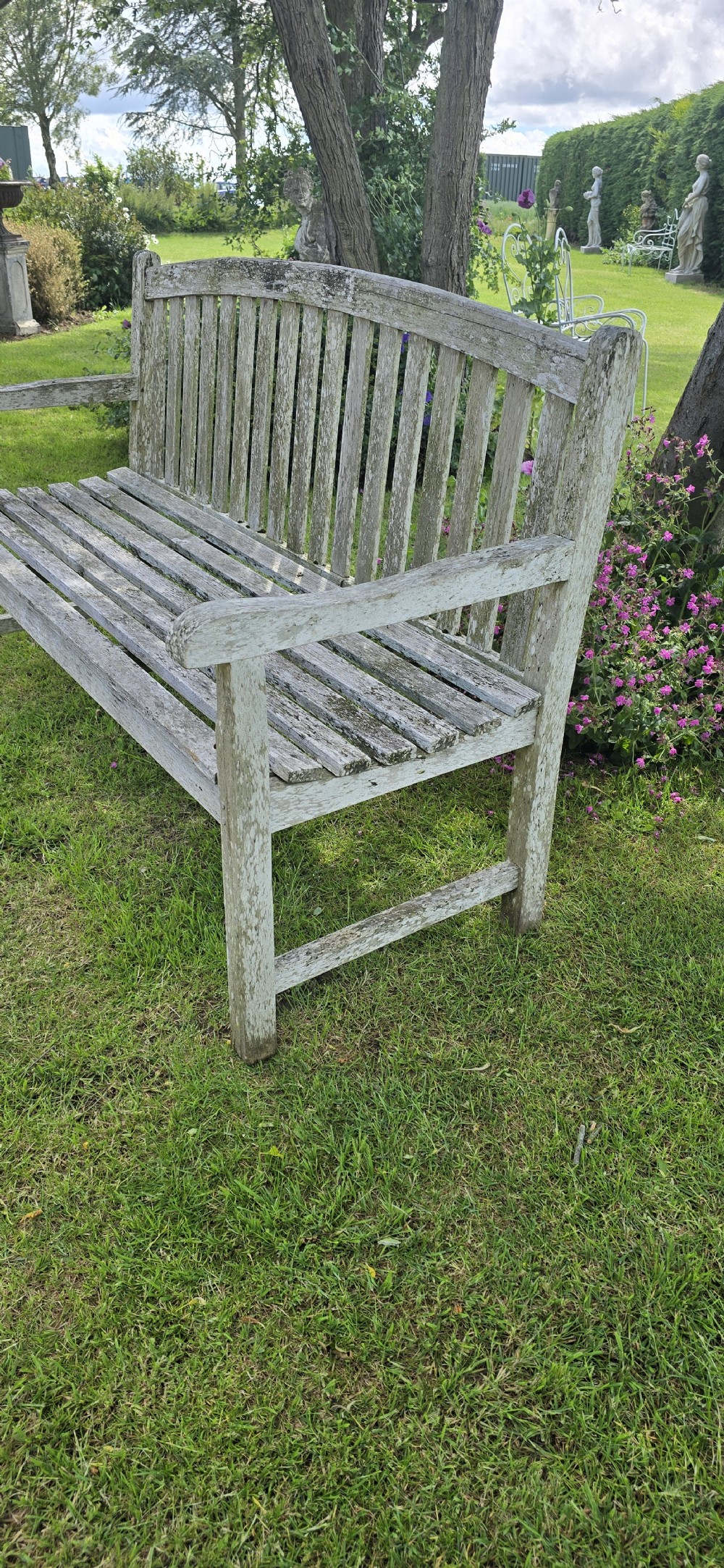 A weathered teak garden bench with a silvered grey patina, featuring vertical back slats, flat armrests, and square legs. View V