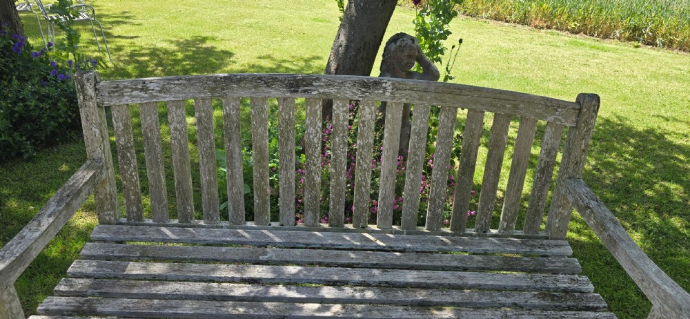 A weathered teak garden bench with a silvered grey patina, featuring vertical back slats, flat armrests, and square legs. View VI