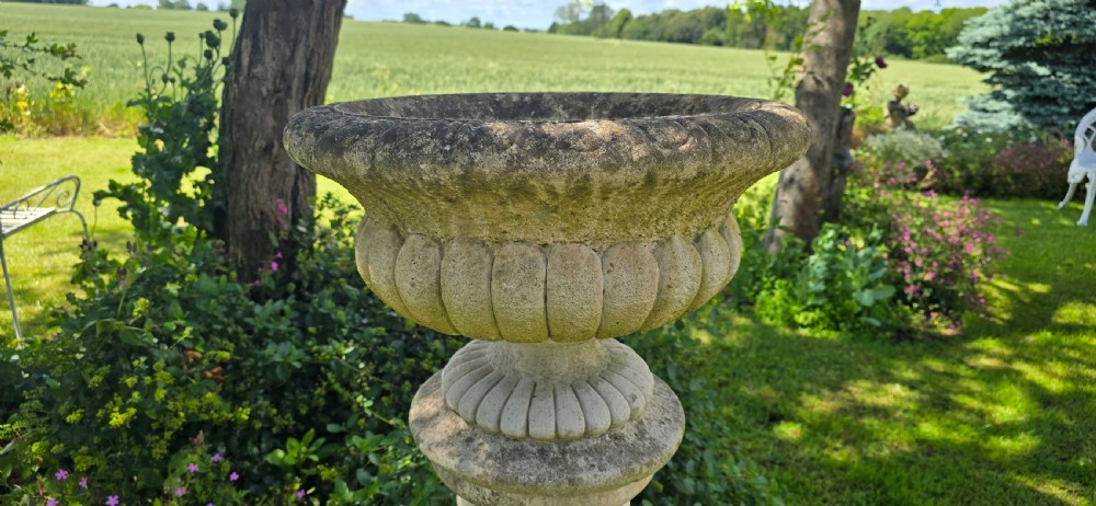 A weathered stone garden urn featuring lobed fluting, elevated on a fluted cylindrical pedestal and square plinth base. View II